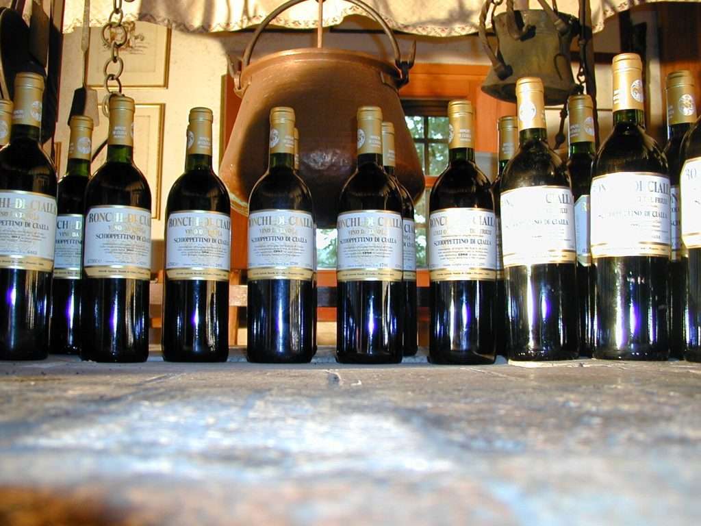 A close row of wine bottles standing on a stone surface in a cellar, labels facing the camera.