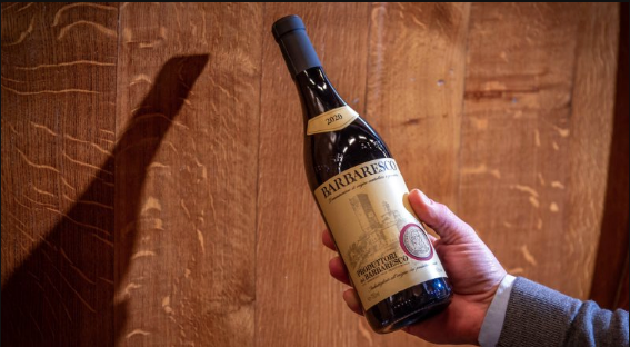 A hand holding an old bottle of wine up against a wooden wall in low light.