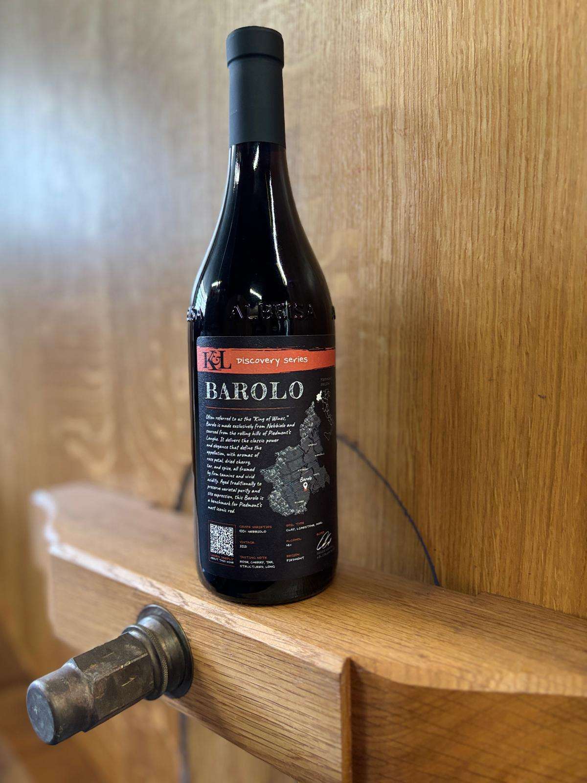 A bottle of Barolo standing on a pale oak shelf beside an old wooden bottle stopper.