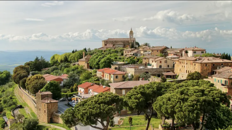 A hill town with a church and stone walls above wooded slopes and umbrella pines.