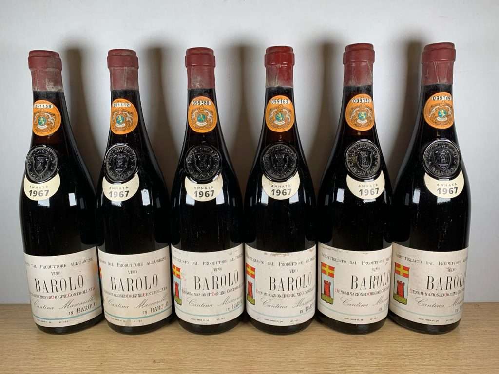 Six bottles of 1967 Barolo standing in a row on a wooden table.