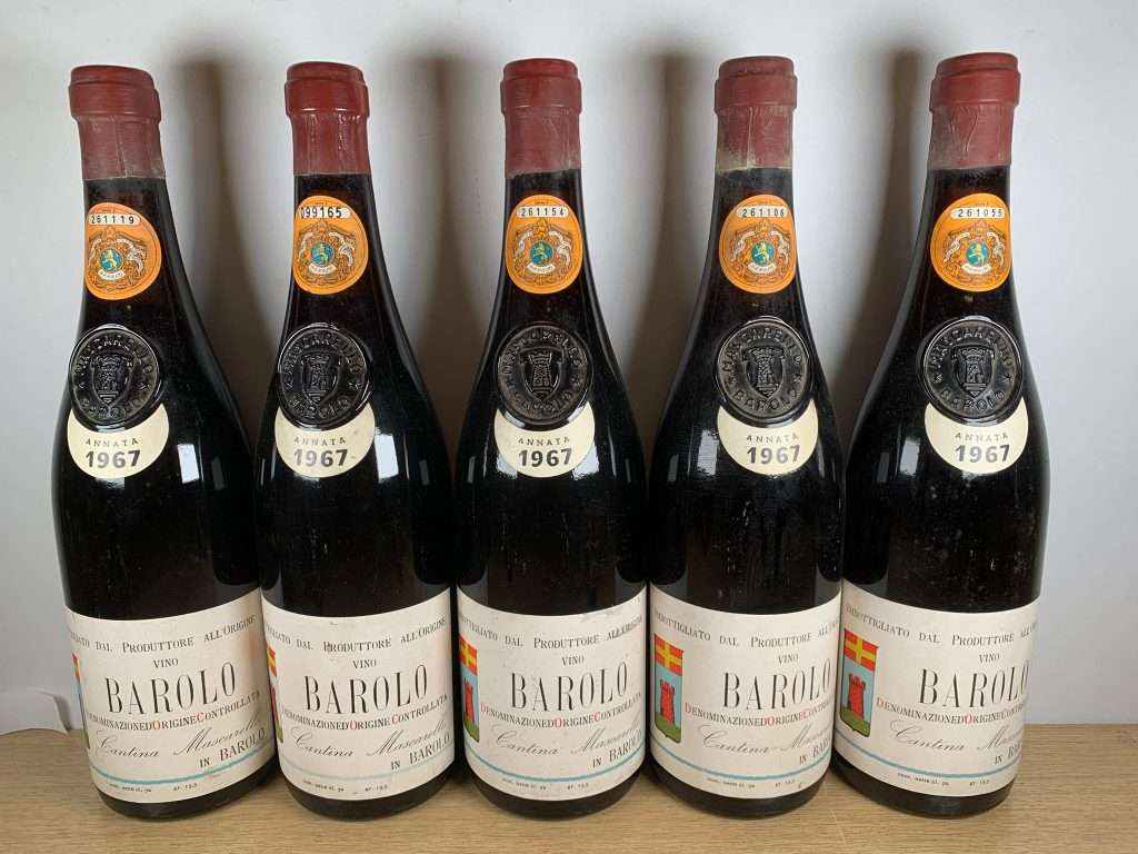 Five bottles of 1967 Barolo arranged in two rows on a wooden table.