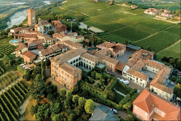 An aerial view of a small brick village with a tower, ringed by vineyards and gardens.