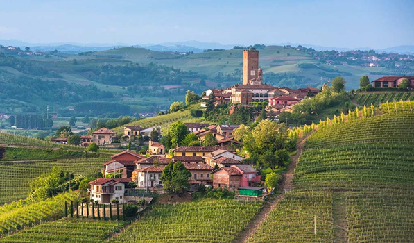 A hill village with a tall bell tower rising above vineyards and orchards, ridges fading behind.