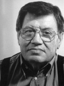 A black and white portrait of a man in glasses and a dark shirt looking at the camera.