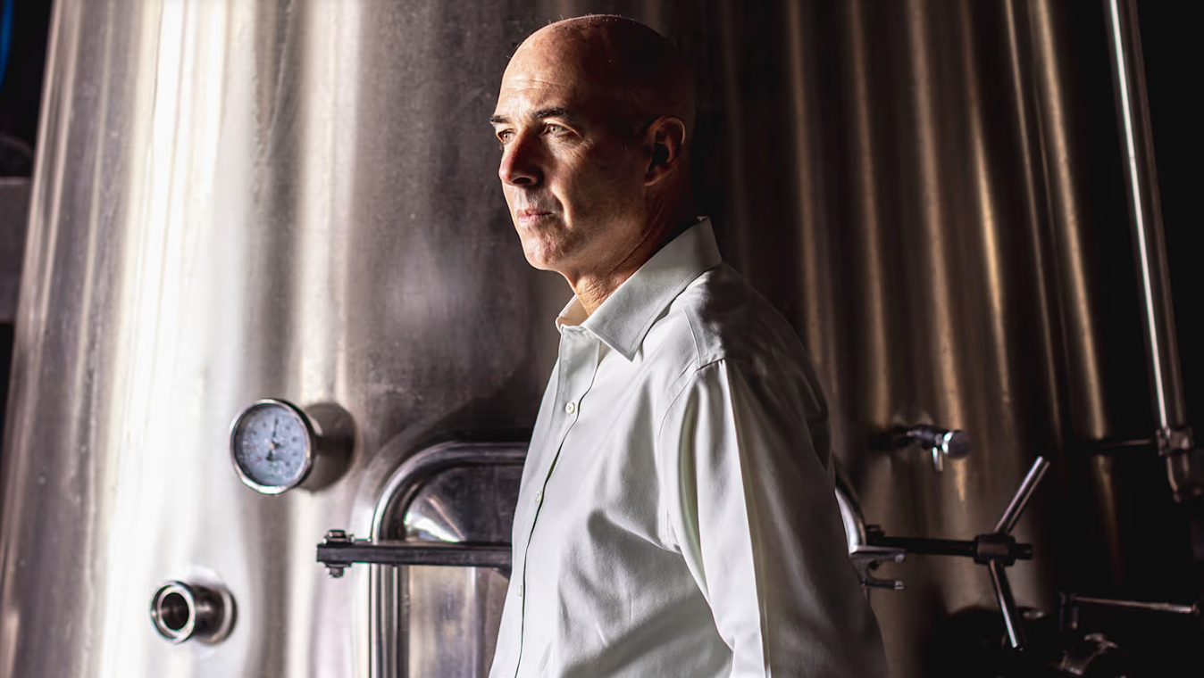 A man in a white shirt standing between stainless steel tanks in a cellar.