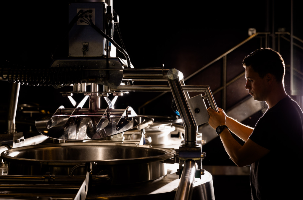 A man in a dark shirt working at a large stainless steel tank under low light.