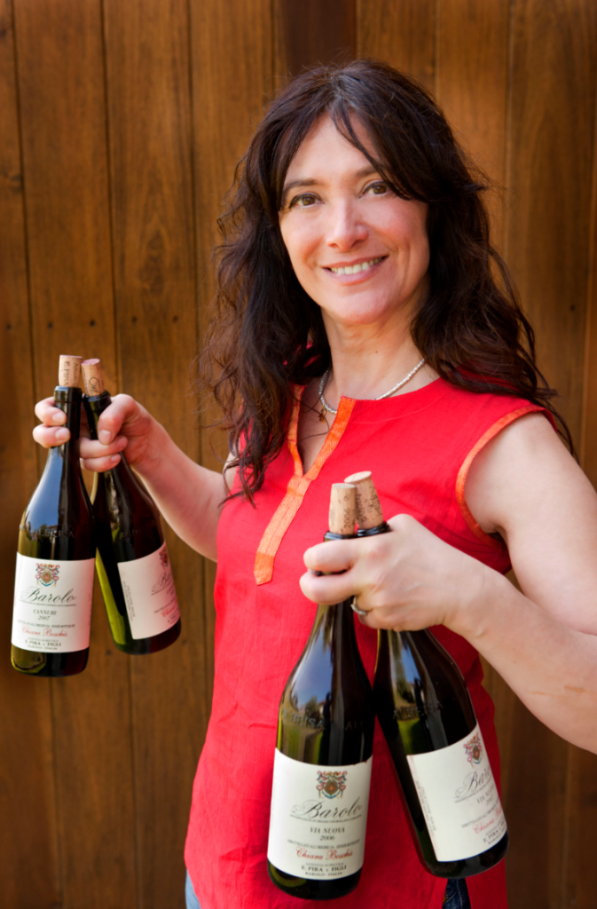 A woman in a red dress holding three bottles of wine, smiling at the camera.