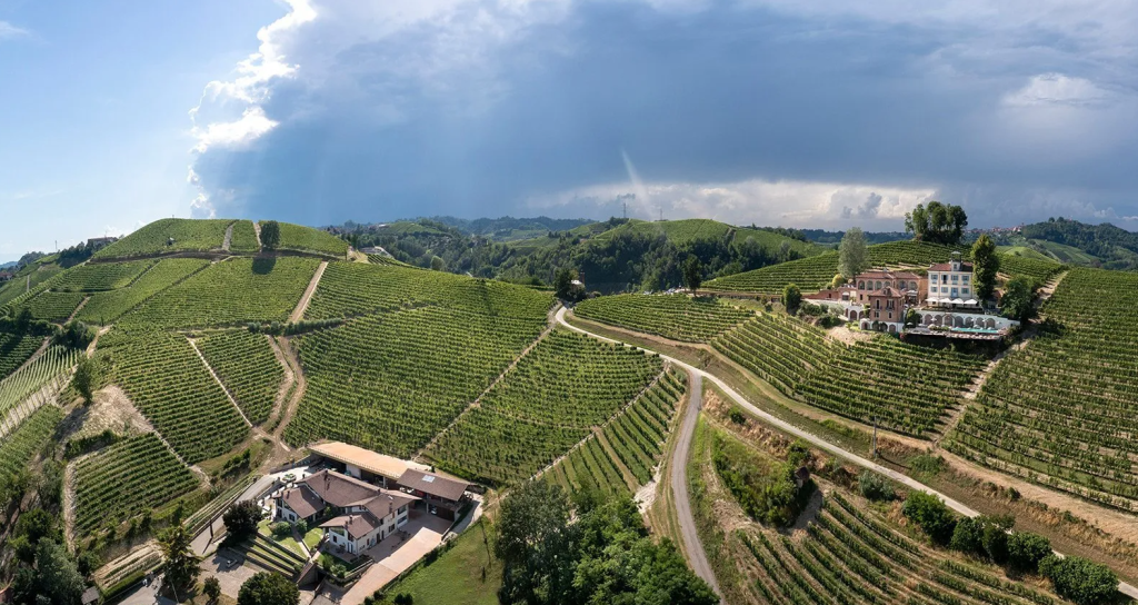 An aerial view of a farm and winery among vineyards, with a rainbow over the ridge behind.